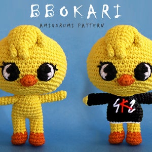Puede incluir: Un patrón de amigurumi de crochet para un pollito amarillo con ojos negros y un pico rojo. El pollito lleva una camiseta negra con texto blanco que dice "SKZ".