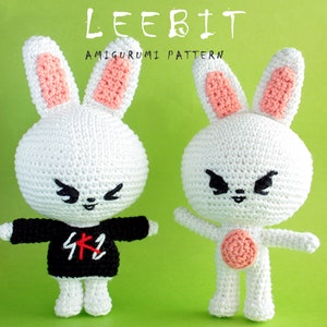 May include: Two white crocheted amigurumi bunny plushies with pink ears. One bunny is wearing a black shirt with a red and white graphic. The other bunny has a pink circle on its belly. The bunnies have black eyes and a black mouth.