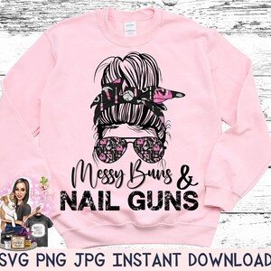May include: A light pink sweatshirt with the text "Messy Buns & Nail Guns" in black. The graphic features a woman's face with sunglasses, a messy bun, and a bandana. The sunglasses have a pattern of tools.