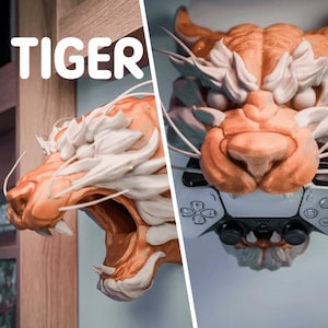 Może przedstawiać: Szczegółowa, pomarańczowo-biała rzeźba głowy tygrysa z kontrolerem. Słowo "TIGER" jest wyświetlane dużymi białymi literami. Pysk tygrysa jest otwarty, odsłaniając ostre zęby. Kontroler jest czarno-biały.