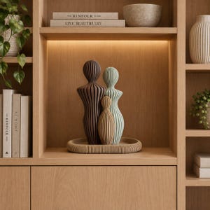 May include: A set of three abstract human-shaped sculptures with a ribbed texture, featuring one large dark brown figure, one medium light green figure, and one small tan figure, all resting on a matching oval ribbed base.
