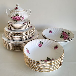 May include: A set of white porcelain dinnerware with a pink rose pattern and gold trim. The set includes plates, bowls, and a sugar bowl.
