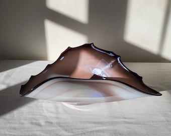 May include: A large, white and brown glass bowl with a wavy, organic shape. The bowl is sitting on a white tablecloth.