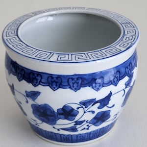 May include: A white ceramic planter with a blue and white floral design. The planter has a geometric pattern around the top rim.