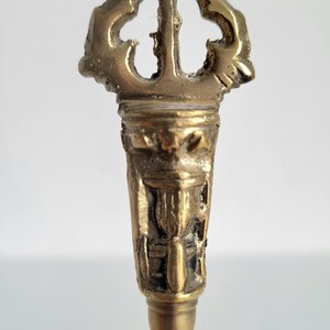May include: A detailed close-up of a brass key with an ornate, openwork design at the top. The key has a textured surface and a decorative handle. The key is a vintage item.