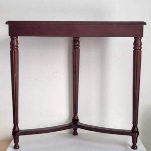 Op de afbeelding: Een bordeauxrode, rechthoekige bijzettafel met vier gedraaide poten. De tafel heeft een eenvoudig, elegant ontwerp, met een licht gebogen bovenrand. De poten zijn gegroefd en taps toelopend. De tafel is ongeveer 76 cm lang.
