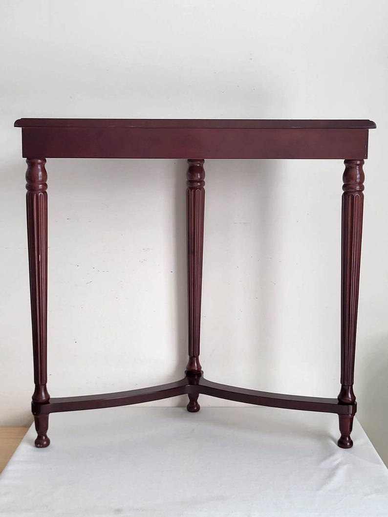 Op de afbeelding: Een bordeauxrode, rechthoekige bijzettafel met vier gedraaide poten. De tafel heeft een eenvoudig, elegant ontwerp, met een licht gebogen bovenrand. De poten zijn gegroefd en taps toelopend. De tafel is ongeveer 76 cm lang.