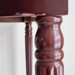 Op de afbeelding: Close-up van een donkerbruine houten tafel. De tafel heeft een rechthoekig blad en sierlijke, gedraaide poten. E&eacute;n poot is een dikke, afgeronde kolom, terwijl een andere een slank, gefluteerd ontwerp heeft. De afwerking van de tafel heeft een rijke, warme tint.