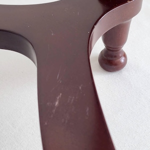 Op de afbeelding: Close-up van een donkerbruine houten tafelpoten en tafelblad. Het tafelblad heeft een gebogen ontwerp met zichtbare krassen. De poot is een gedraaid ontwerp met een bolvormige voet. Het hout heeft een glanzende afwerking.