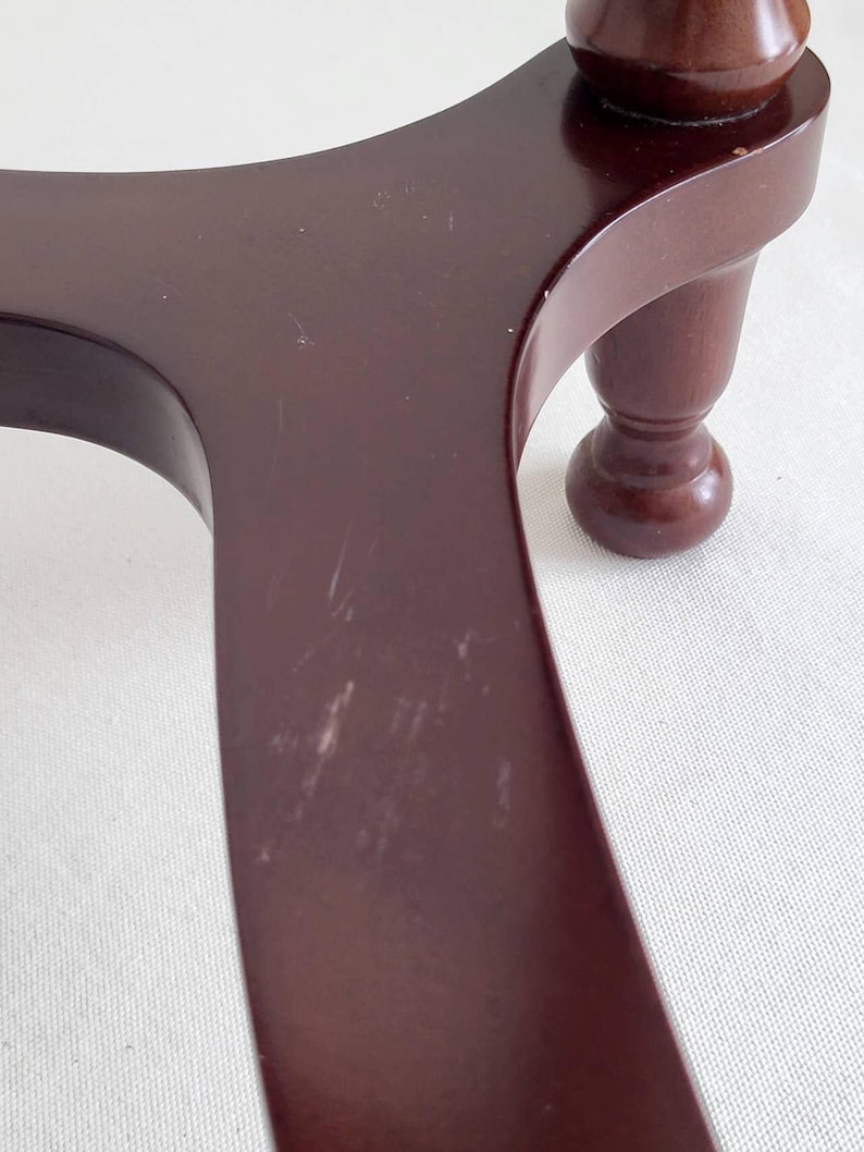 Op de afbeelding: Close-up van een donkerbruine houten tafelpoten en tafelblad. Het tafelblad heeft een gebogen ontwerp met zichtbare krassen. De poot is een gedraaid ontwerp met een bolvormige voet. Het hout heeft een glanzende afwerking.