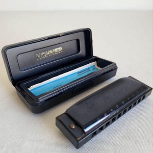 May include: A black Hohner Pro Harp harmonica with its open black case. The harmonica has the words "Pro Harp" printed on it, along with numbers. The case has the word "Hohner" printed on it.