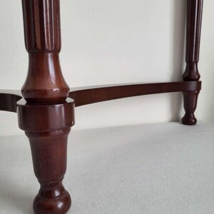 Op de afbeelding: Een close-up van een donkerbruine houten tafel met een decoratieve, gegroefde poot. De poot heeft een bolvorm en een afgeronde voet. De horizontale steun van de tafel is ook zichtbaar, waardoor een klassiek meubelontwerp ontstaat.