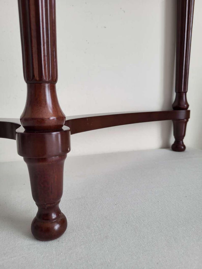 Op de afbeelding: Een close-up van een donkerbruine houten tafel met een decoratieve, gegroefde poot. De poot heeft een bolvorm en een afgeronde voet. De horizontale steun van de tafel is ook zichtbaar, waardoor een klassiek meubelontwerp ontstaat.