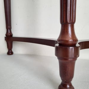 Op de afbeelding: Close-up van een donkerbruine houten tafel met een cannelure pootontwerp. De tafel heeft een klassieke, elegante stijl, met een gebogen steunbalk die de poten verbindt. De poten zijn aan de basis afgerond.