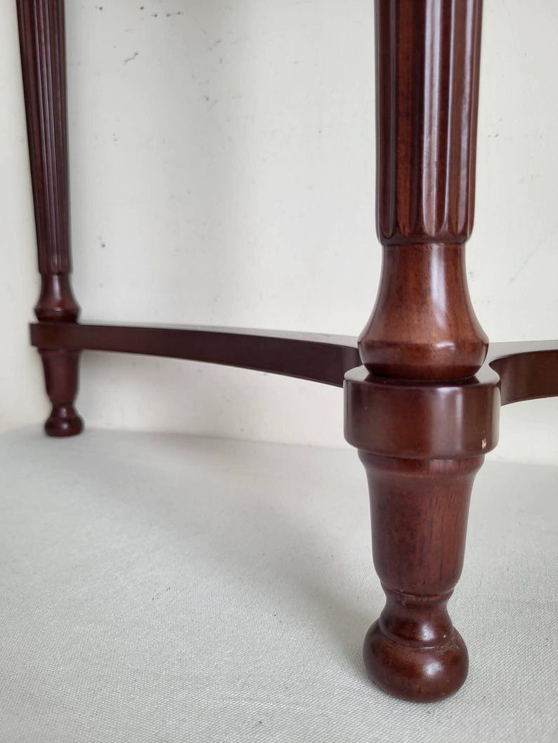 Op de afbeelding: Close-up van een donkerbruine houten tafel met een cannelure pootontwerp. De tafel heeft een klassieke, elegante stijl, met een gebogen steunbalk die de poten verbindt. De poten zijn aan de basis afgerond.