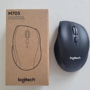 May include: A black Logitech M705 customizable mouse next to its cardboard box. The box has the model number and the Logitech logo. The mouse has a scroll wheel and two buttons. The box reads "Customizable Mouse" and "Souris personnalisable".