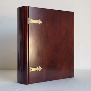 Peut inclure: Un meuble en bois brun foncé avec une colonne vertébrale incurvée et des charnières en laiton. Le meuble a une finition lisse et polie et une forme rectangulaire. Les charnières en laiton sont décoratives et ajoutent une touche d'élégance.