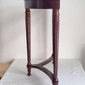 Op de afbeelding: Een donker bordeauxrode, halfronde bijzettafel met een driepoot. De tafel heeft een glad, gepolijst oppervlak en decoratieve, gefreesde poten. De tafel is ongeveer 76 cm hoog.