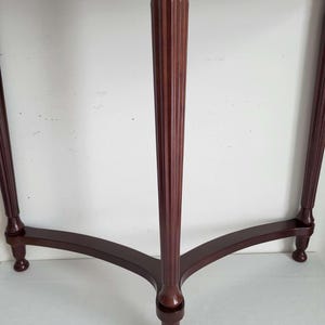 Op de afbeelding: Een donkerbruine houten bijzettafel met een rond blad en drie poten. De centrale poot is gegroefd en de tafel heeft een klassiek, elegant ontwerp. De poten zijn gebogen en eindigen in kleine, afgeronde voetjes.