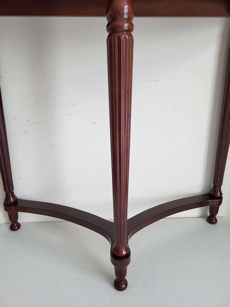Op de afbeelding: Een donkerbruine houten bijzettafel met een rond blad en drie poten. De centrale poot is gegroefd en de tafel heeft een klassiek, elegant ontwerp. De poten zijn gebogen en eindigen in kleine, afgeronde voetjes.