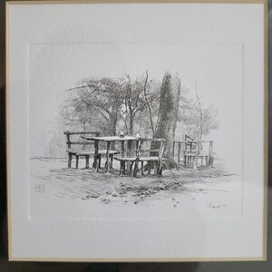 May include: A black and white pen and ink drawing of a table and chairs under a tree. The drawing is framed in a black frame.