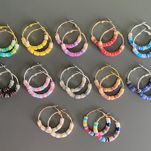 Puede incluir: Doce pares de pendientes de aro con cuentas de plástico de colores superpuestas. Los pendientes están hechos de metal dorado y plateado.