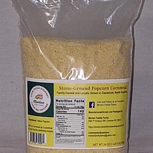 May include: A clear plastic bag filled with stone-ground popcorn cornmeal. The bag has a yellow label with text that reads "Stone-Ground Popcorn Cornmeal" and "Family-Owned and Locally Grown." The net weight is 24 oz (1 lb 8 oz).