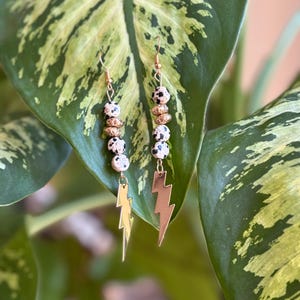 May include: A pair of gold dangle earrings with black and white dalmatian jasper beads and gold lightning bolt charms.
