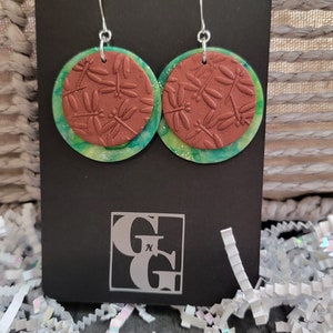 May include: Handmade earrings with a green and brown dragonfly design. The earrings are on a black card with the text "HANDMADE EARRINGS".