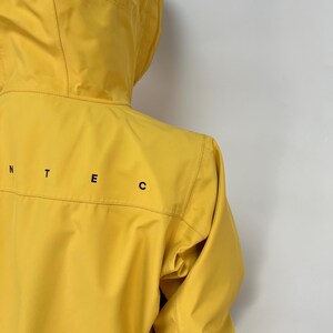 May include: A bright yellow hooded jacket with black lettering on the back. The jacket has a zipper closure and a drawstring hood. The jacket is made of a lightweight material and appears to be water-resistant.