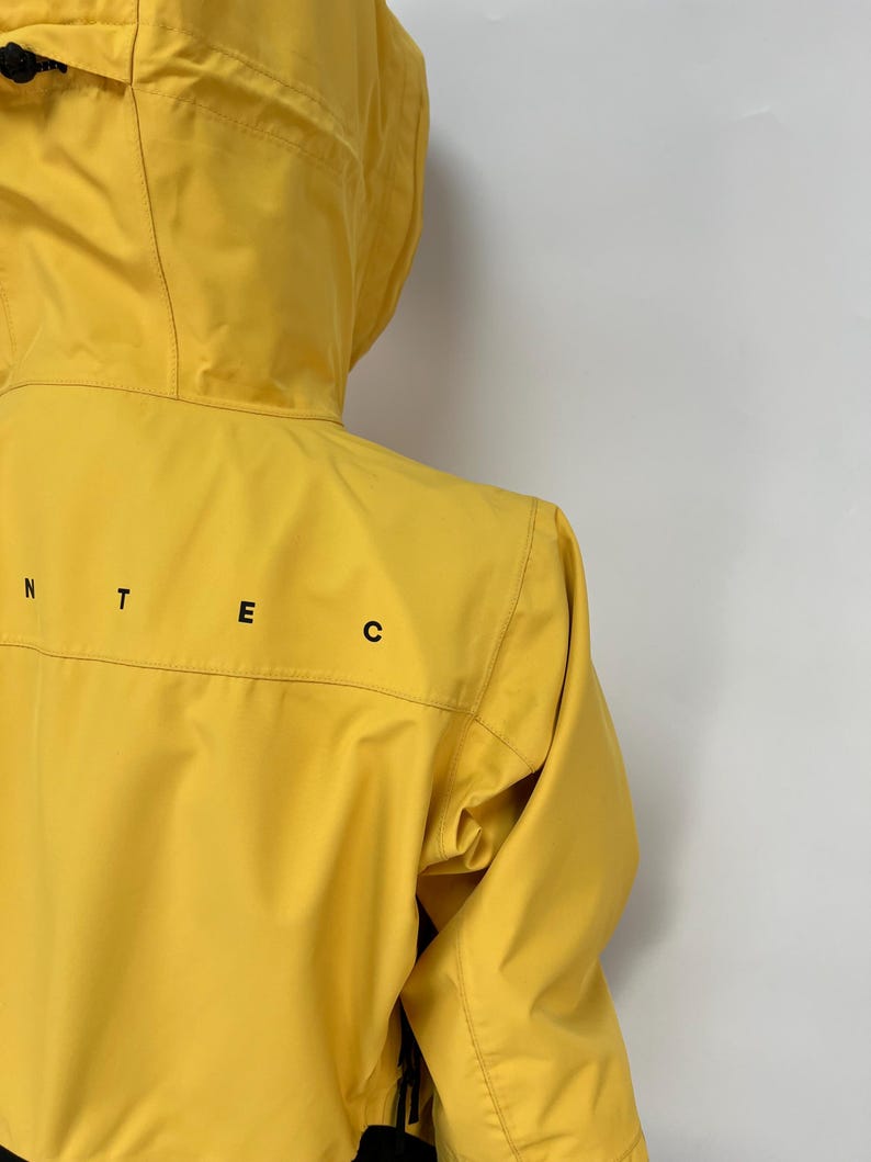 May include: A bright yellow hooded jacket with black lettering on the back. The jacket has a zipper closure and a drawstring hood. The jacket is made of a lightweight material and appears to be water-resistant.