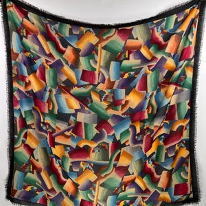 Peut inclure: Une écharpe à motifs abstraits colorés avec une bordure en franges noires. L'écharpe présente un motif géométrique avec des nuances de rouge, jaune, vert, bleu et violet.