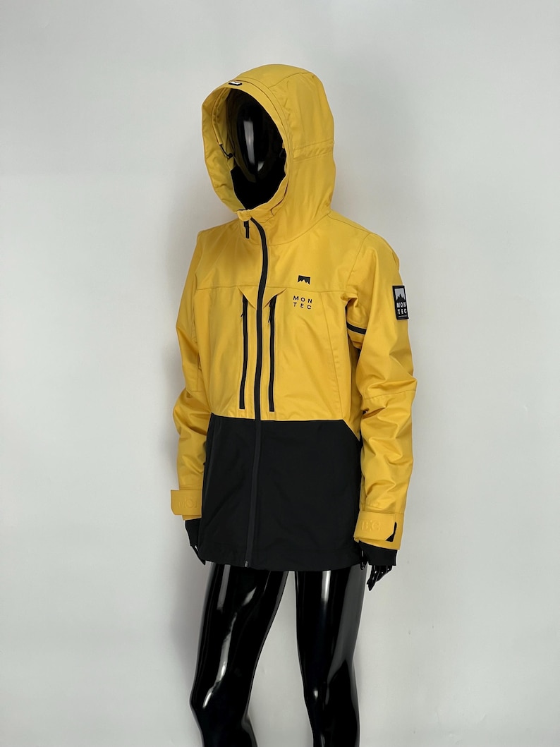 May include: A yellow and black hooded jacket with the text "MONTEC" on the chest. The jacket has a zip-up front, black accents, and a small logo patch on the sleeve. The jacket is displayed on a mannequin.