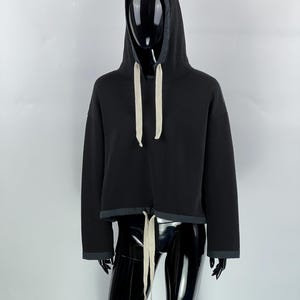 May include: Black cropped hoodie with a drawstring hood and long sleeves. The hoodie has a white drawstring.