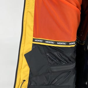 May include: Close-up of a yellow and black winter jacket interior. The jacket features a bright orange lining and a black pocket. The brand name "MONTEC" is printed on a black band. The jacket is designed for cold weather.