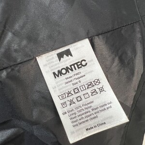 May include: A close-up of a black jacket's interior with a white tag. The tag reads "MONTEC" and includes washing instructions, size "S", and fabric details: 100% polyester shell and 100% nylon lining. The jacket is made in China.