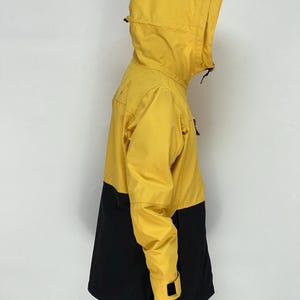 May include: A yellow and black hooded jacket. The upper portion of the jacket, including the hood and sleeves, is yellow. The lower portion of the jacket is black. The jacket has a zipper closure and a drawstring hood.
