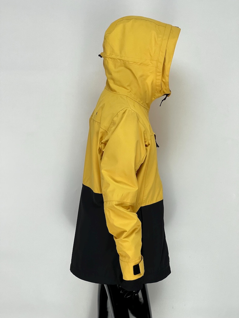 May include: A yellow and black hooded jacket. The upper portion of the jacket, including the hood and sleeves, is yellow. The lower portion of the jacket is black. The jacket has a zipper closure and a drawstring hood.
