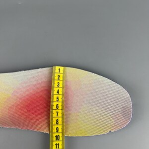 May include: A colorful shoe insole with a gradient of pink, yellow, and white. A yellow measuring tape is placed next to the insole, showing a measurement of approximately 5 inches.