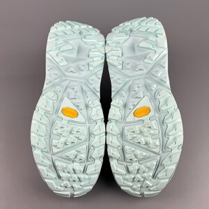 May include: A pair of light blue hiking shoes, soles facing up, with a textured pattern and the brand name "Vibram" in yellow. The shoes are designed for outdoor activities and provide grip and support.