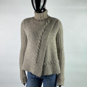 May include: A gray, cable knit sweater with a turtleneck and a diagonal design. The sweater is made of a soft, fuzzy material.