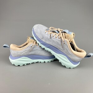 May include: A pair of athletic shoes in a light gray color with light blue and tan accents. The soles are light green. The shoes are designed for outdoor activities and have a textured upper.