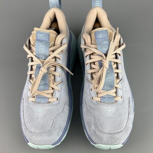 May include: A pair of light gray suede sneakers with light blue and tan accents. The sneakers have light blue soles and laces, with a padded tongue and collar. The shoes are designed for athletic activities and casual wear.