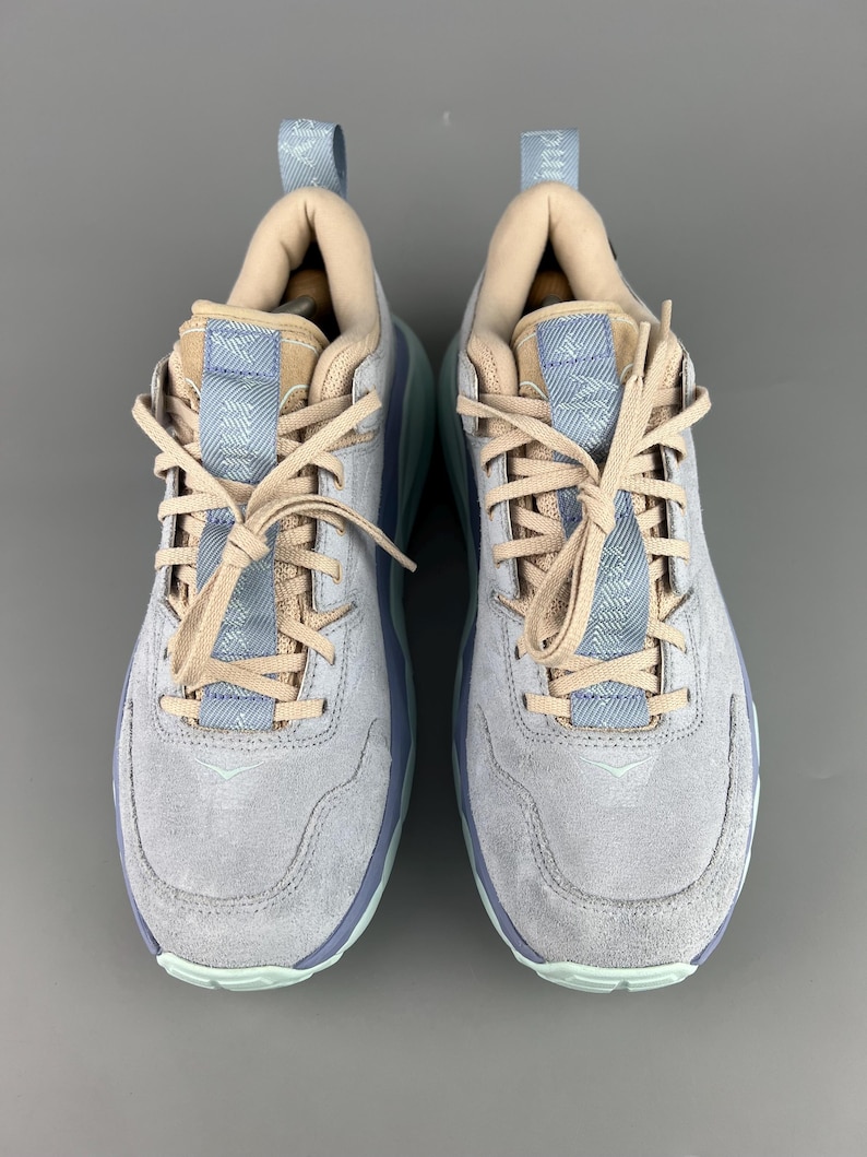 May include: A pair of light gray suede sneakers with light blue and tan accents. The sneakers have light blue soles and laces, with a padded tongue and collar. The shoes are designed for athletic activities and casual wear.