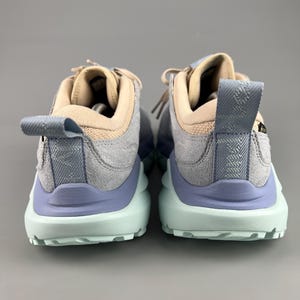 May include: A pair of athletic shoes with a light blue, gray, and tan color scheme. The shoes have a textured design on the heel and a light green sole. The laces are tan.
