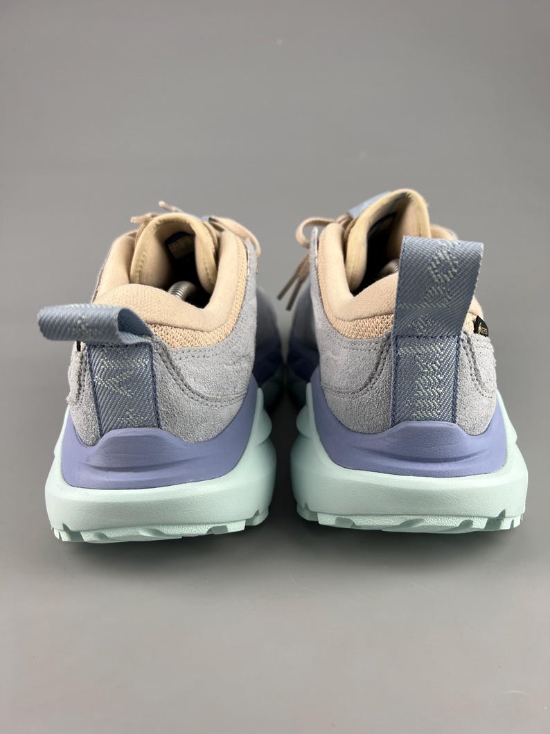 May include: A pair of athletic shoes with a light blue, gray, and tan color scheme. The shoes have a textured design on the heel and a light green sole. The laces are tan.