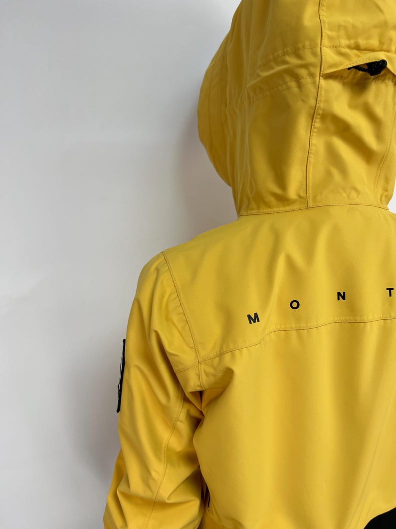 May include: A bright yellow hooded jacket with the word "MONT" printed in black on the back. The jacket has a hood and a black patch on the left sleeve. The jacket is made of a smooth, possibly waterproof material.