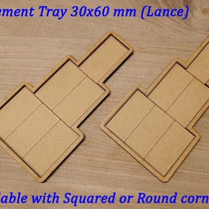 Może przedstawiać: Dwa drewniane tace do ruchu, każda z czterema przegródkami, o wymiarach 30x60 mm. Tace są jasnobrązowe i dostępne z kwadratowymi lub zaokrąglonymi narożnikami. "Movement Tray 30x60 mm (Lance)" jest napisane niebieskim tekstem u góry obrazu.