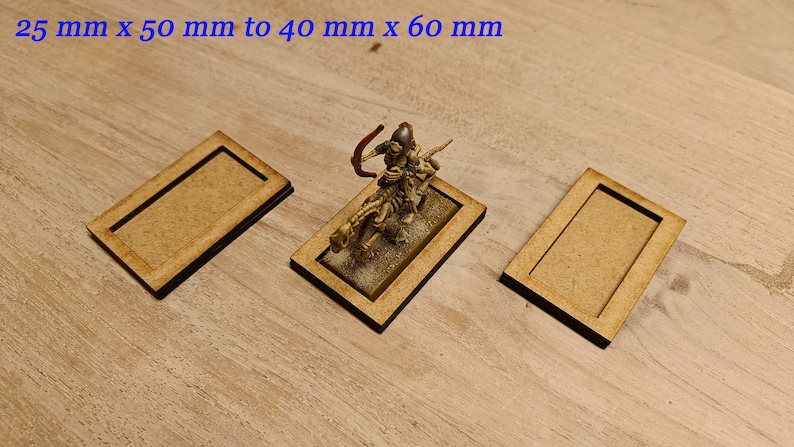May include: Three wooden bases for miniature figures, measuring 25 mm x 50 mm to 40 mm x 60 mm. The bases are made of light brown wood and have a raised edge.