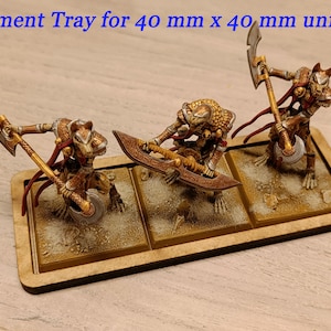 Puede incluir: Una bandeja de movimiento de madera para unidades de 40 mm x 40 mm. La bandeja tiene tres compartimentos, cada uno con una base pintada de color arena. Tres figuras en miniatura est&aacute;n de pie en la bandeja, cada una con un arma diferente.
